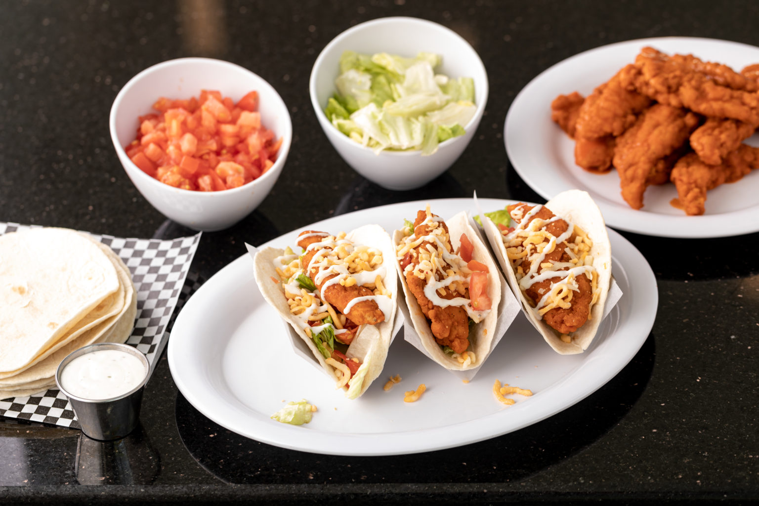 Fried chicken tacos, tortillas, fried chicken, side of chopped tomatoes, side of chopped lettuce
