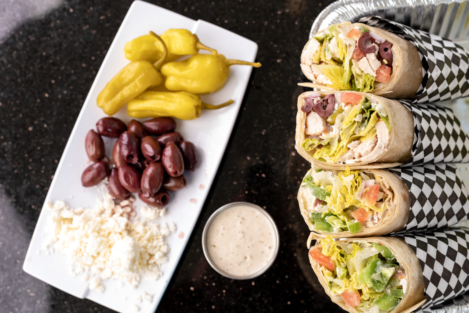 Greek chicken wraps with feta, olives, and pepperoncinis on a plate