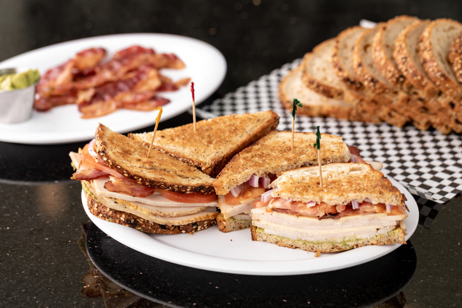 Sandwiches with bread, bacon, and avocado in the background