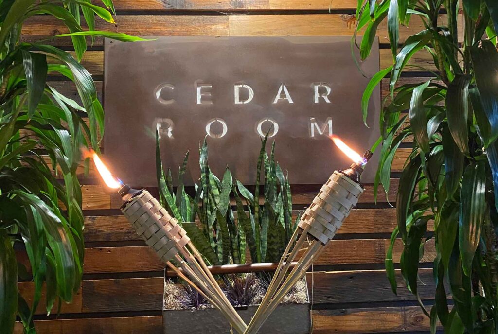 The Cedar Room sign with tiki torches and plants