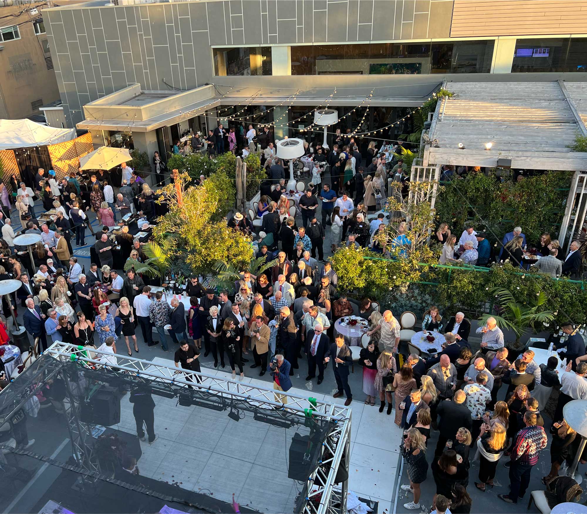 People sitting and standing around tables at a outdoor venue